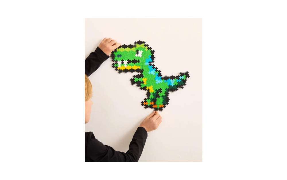 Child assembling a colorful Plus Plus dinosaur jigsaw puzzle shaped like a green dinosaur